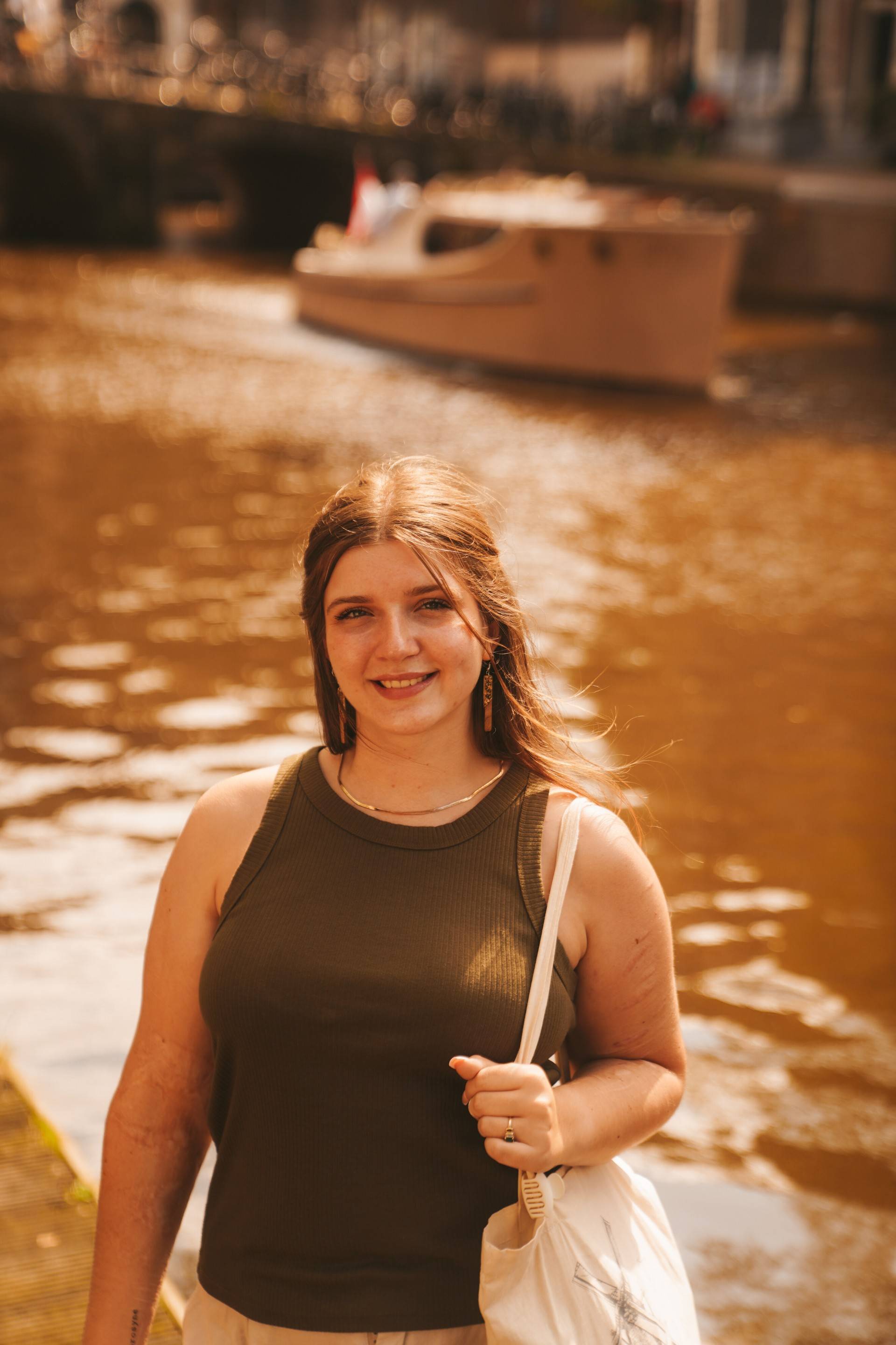 Girl with brown hair, and green tank top smiling at camera with water a boat in the background